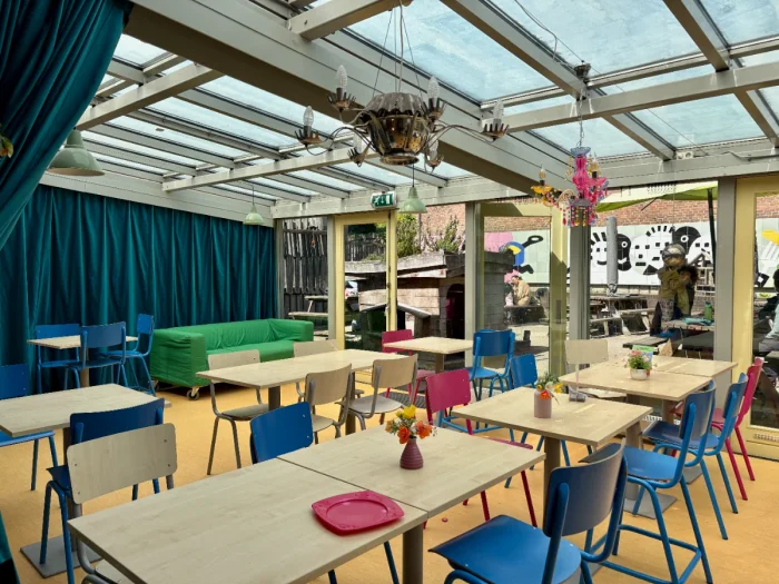 Indoor cafe seating with glass greenhouse ceiling and colorful chairs with view onto outdoor patio