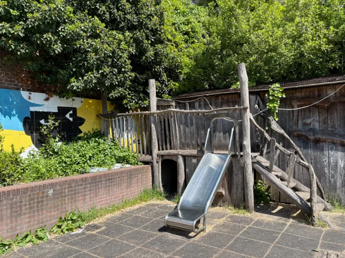 Wooden play structure with slide net to a flower bed and colorful wall mural