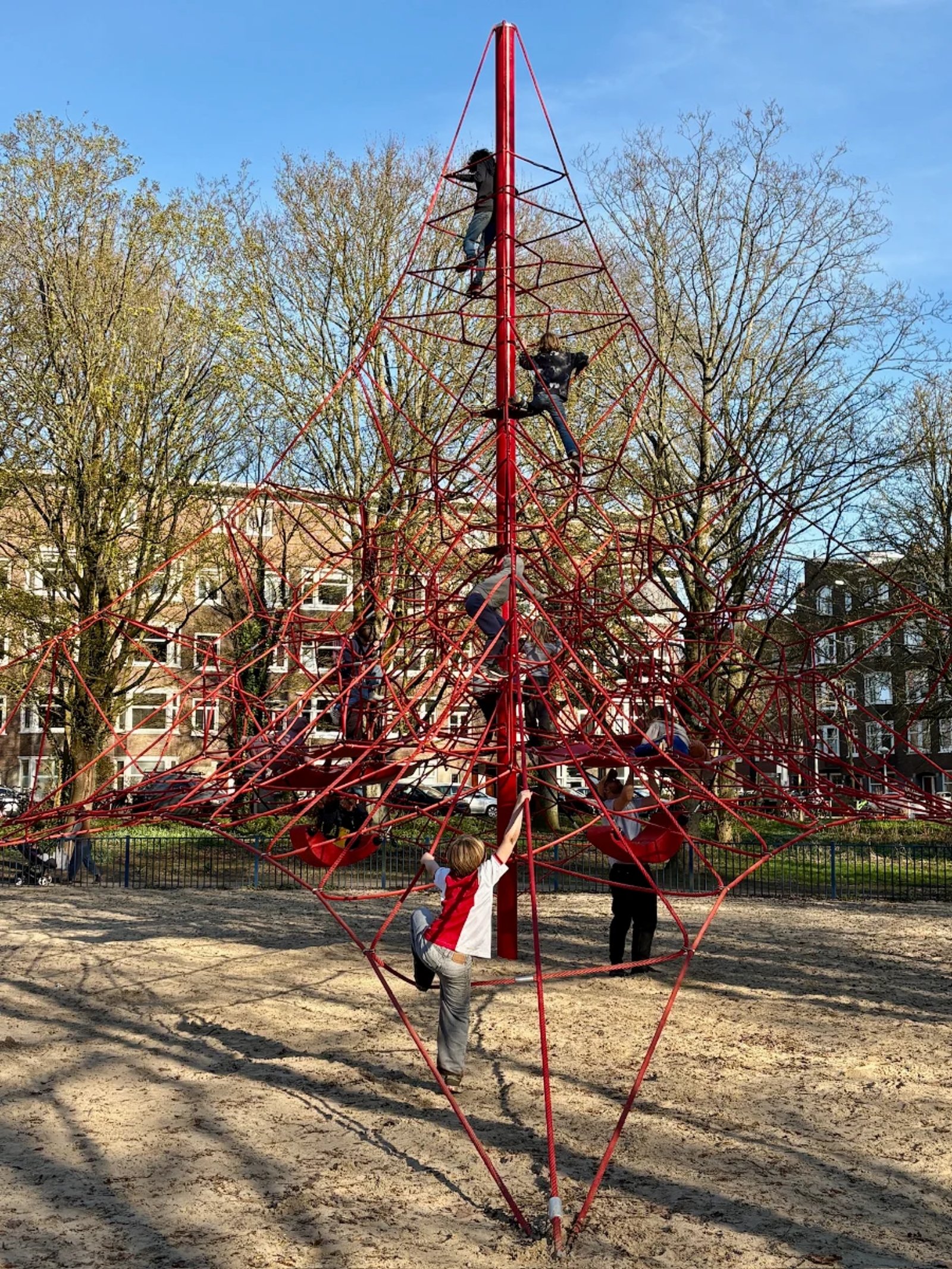 Kids climbing on a tall pyramid-shaped tower with red ropes