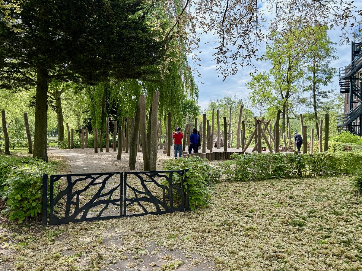 Gate leading to shaded playground with wooden elements and mature trees