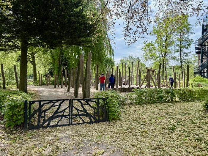 Gate leading to shaded playground with wooden elements and mature trees