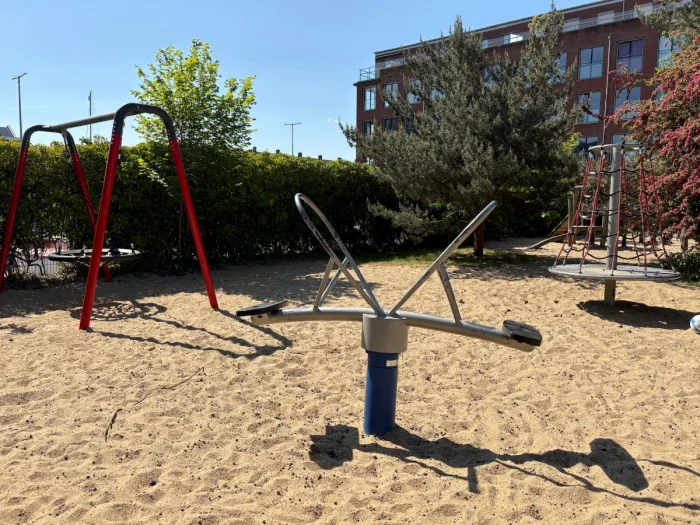 Red nest swing, metal see saw, and climbing pyramid on sunny sand