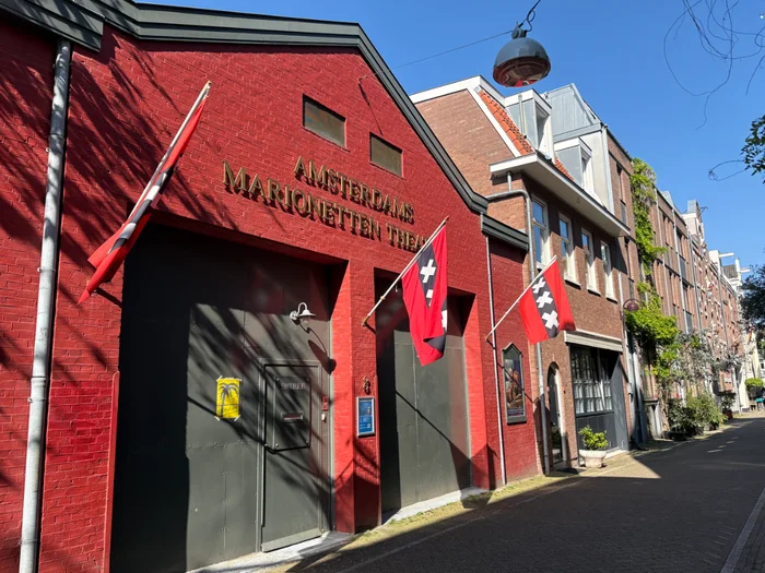 Red painted brick building with gold letter sign above entrance and three Amsterdam flags