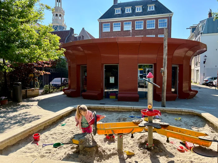 Red round community center building with girl playing in a sandbox outside