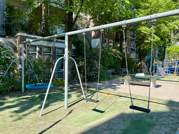 Swing set with nest swing and two standard swings on playground in residential courtyard 