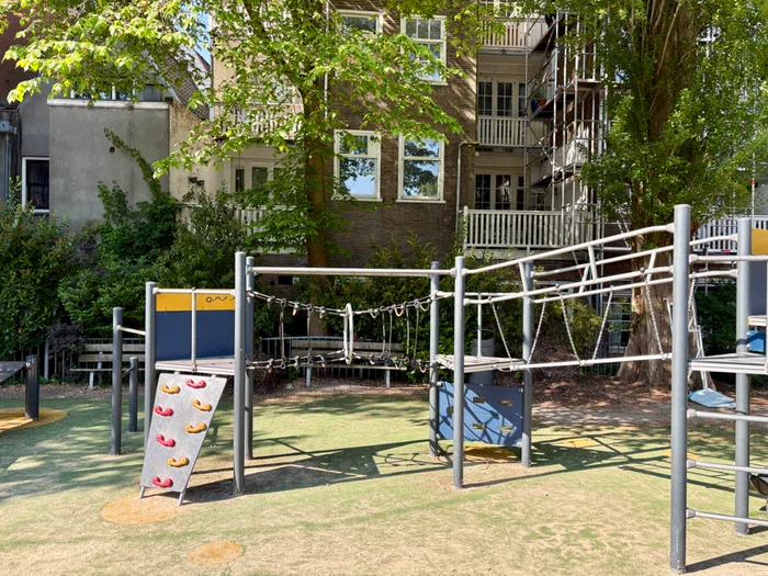 Modern play structure with climbing ramp, rope tunnel bridge, and ladder