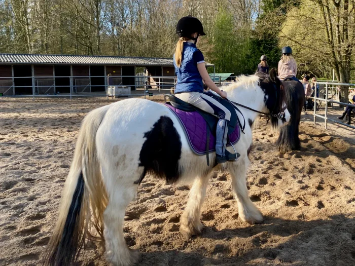 Girl wearing riding helmet and boots riding a black and white pony