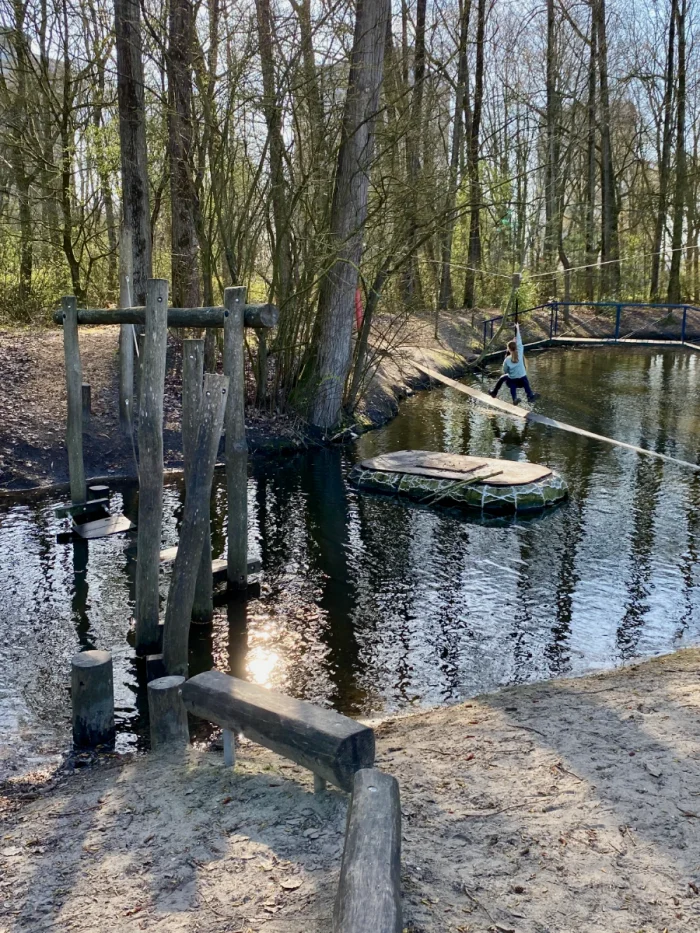 Nature playground with water obstacle course and zipline over river in wooded area