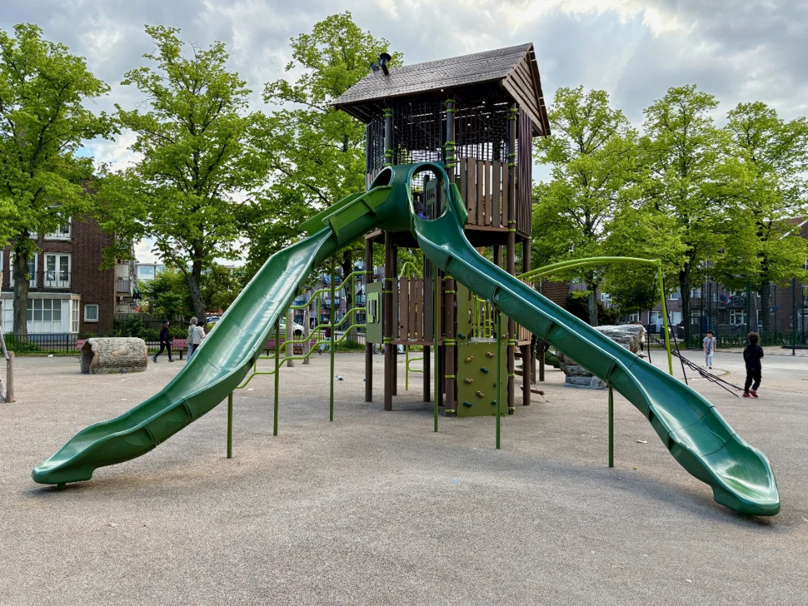 Large climbing house structure with two long green slides winding down with trees behind