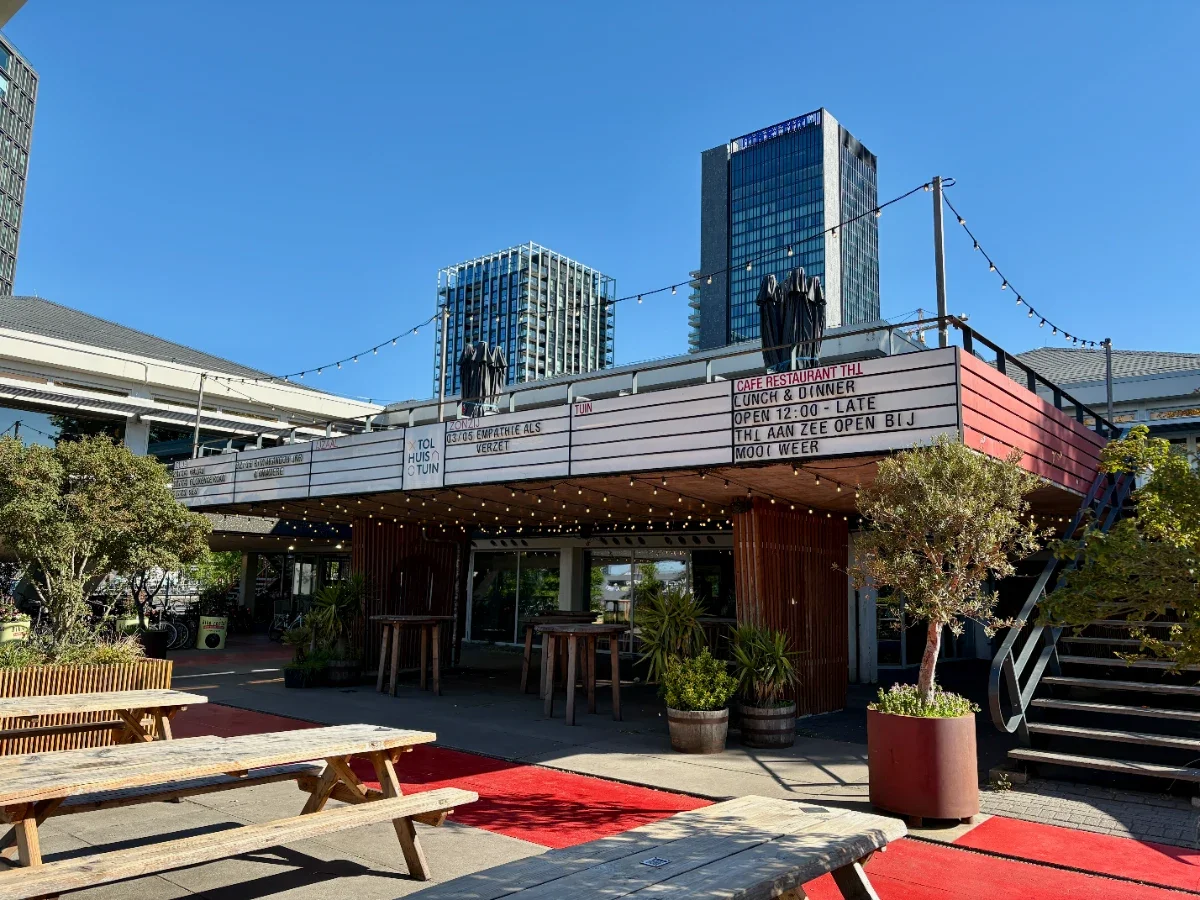 Concert venue with marquee above entrance and large sunny terrace with picnic tables