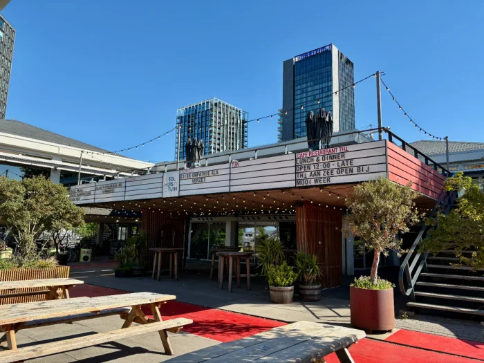 Concert venue with marquee above entrance and large sunny terrace with picnic tables