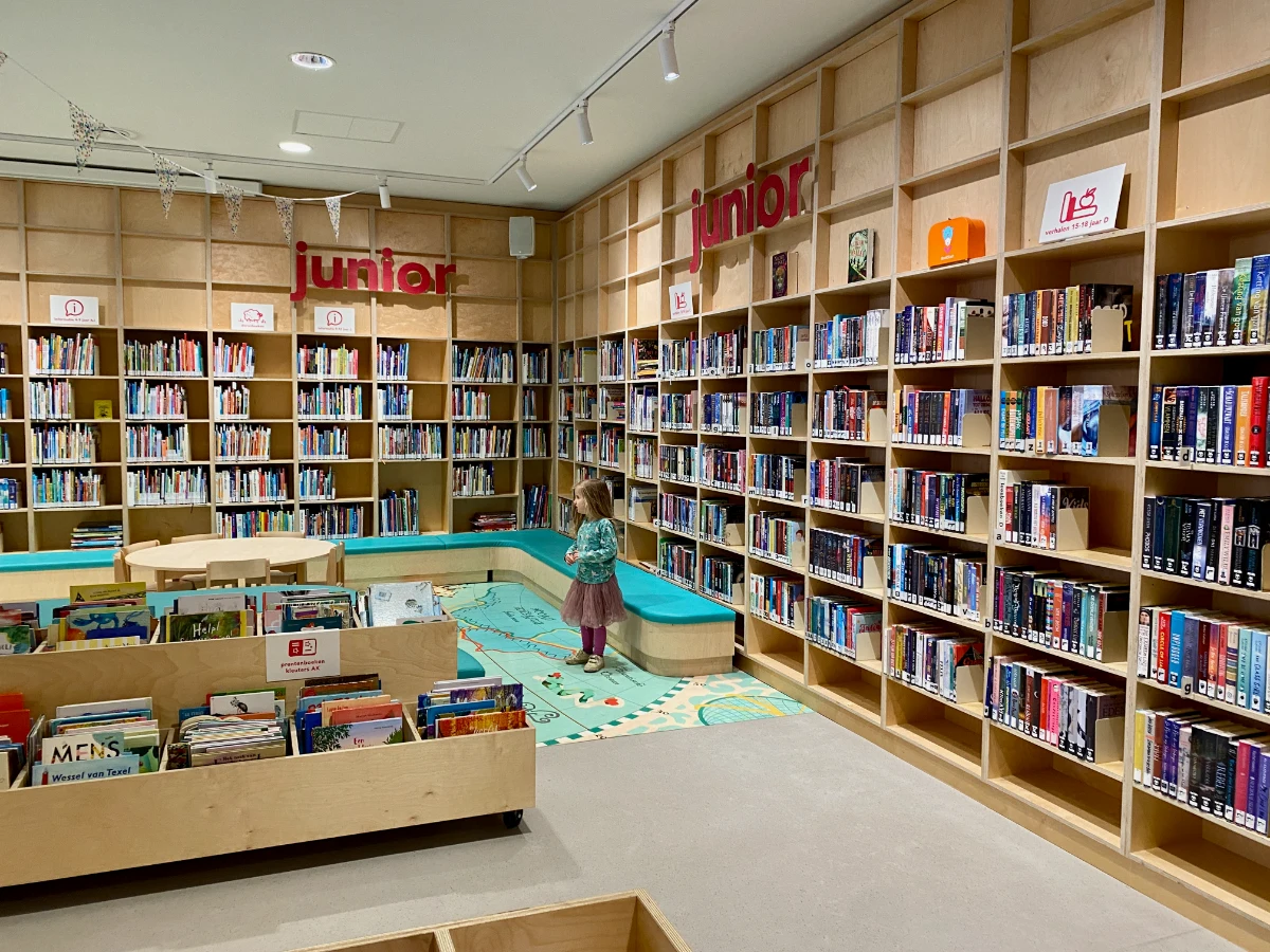 Girl in the children's section of the library with tall bookshelves on the walls and map illustration on the ground