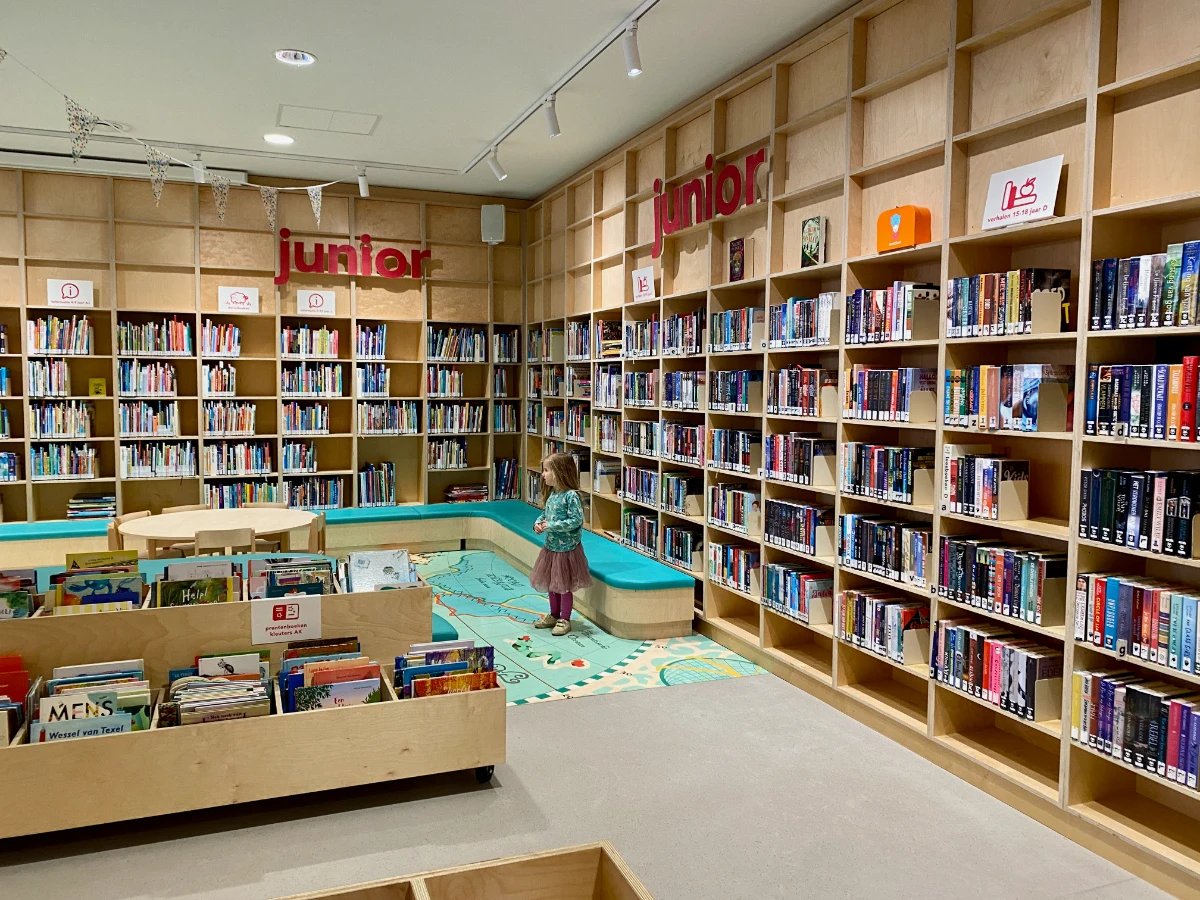 Girl in the children's section of the library with tall bookshelves on the walls and map illustration on the ground