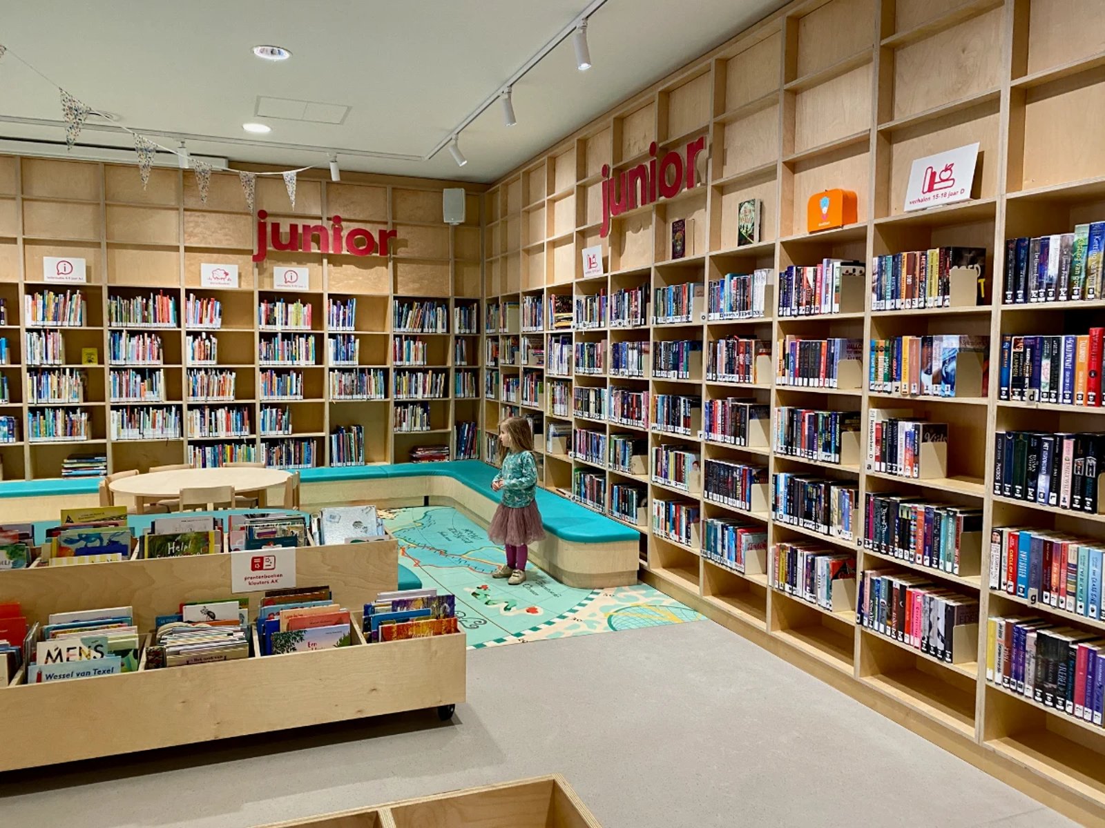 Girl in the children's section of the library with tall bookshelves on the walls and map illustration on the ground