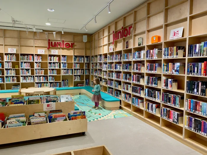 Girl in the children's section of the library with tall bookshelves on the walls and map illustration on the ground
