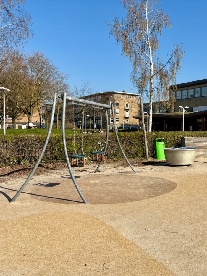 Swing with two baby seats and metal frame on a playground on a bright sunny day