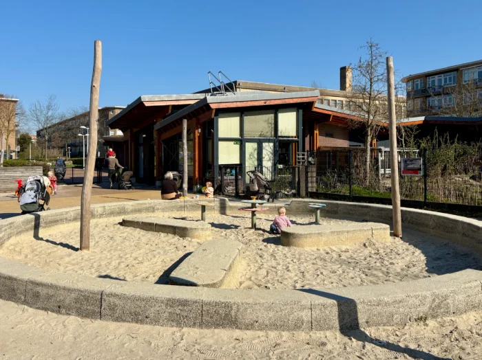 Child plays in a large round sand box with community center behind