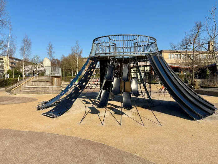Round outdoor playground structure with climbing nets and rubber and metal slides on all sides 