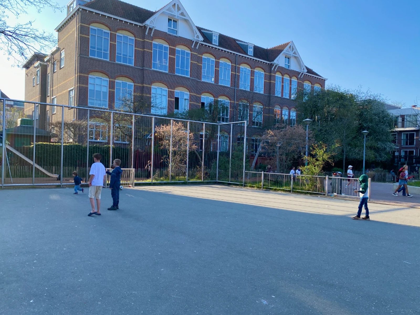 Kids playing on kid-sized enclosed football pitch with residential buildings behind