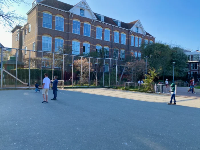 Kids playing on kid-sized enclosed football pitch with residential buildings behind