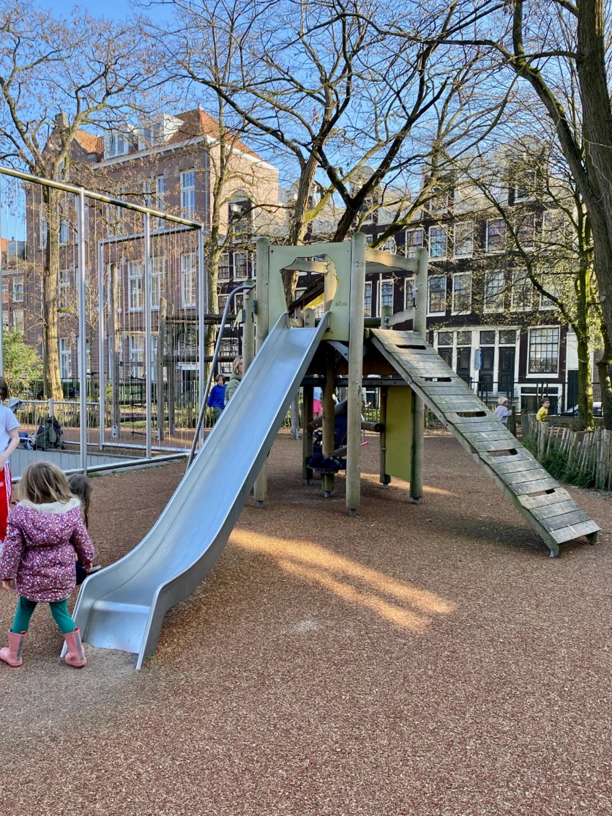 Kids playing on wooden climbing tower with slide and ladder with residential buildings behind