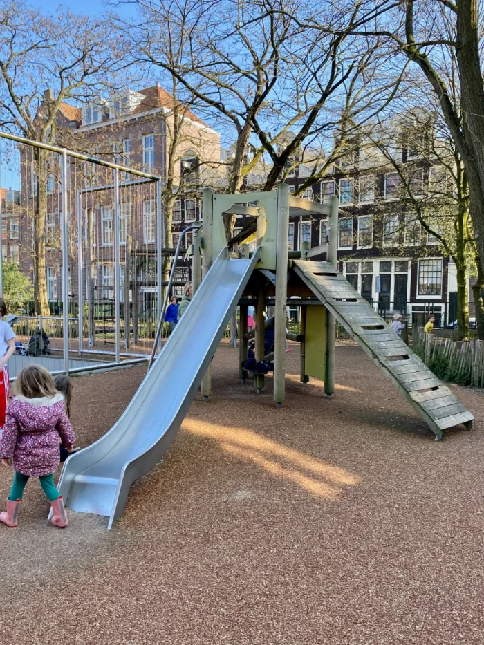 Kids playing on wooden climbing tower with slide and ladder with residential buildings behind