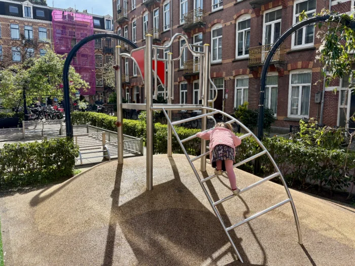 Girl climbing ladder of modern metal climbing structure with mini football pitch behind
