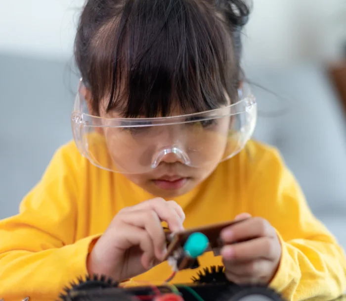 Young girl with yellow shirt and clear safety goggles working on an electronic vehicle