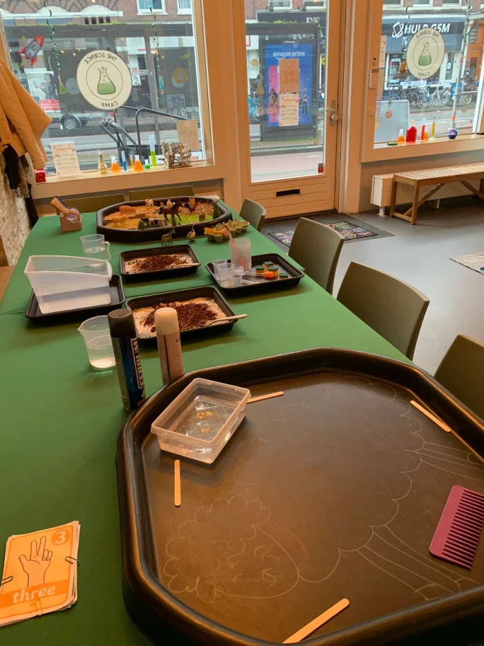 Table set up for a children's science experiment with green table cloth and big windows behind