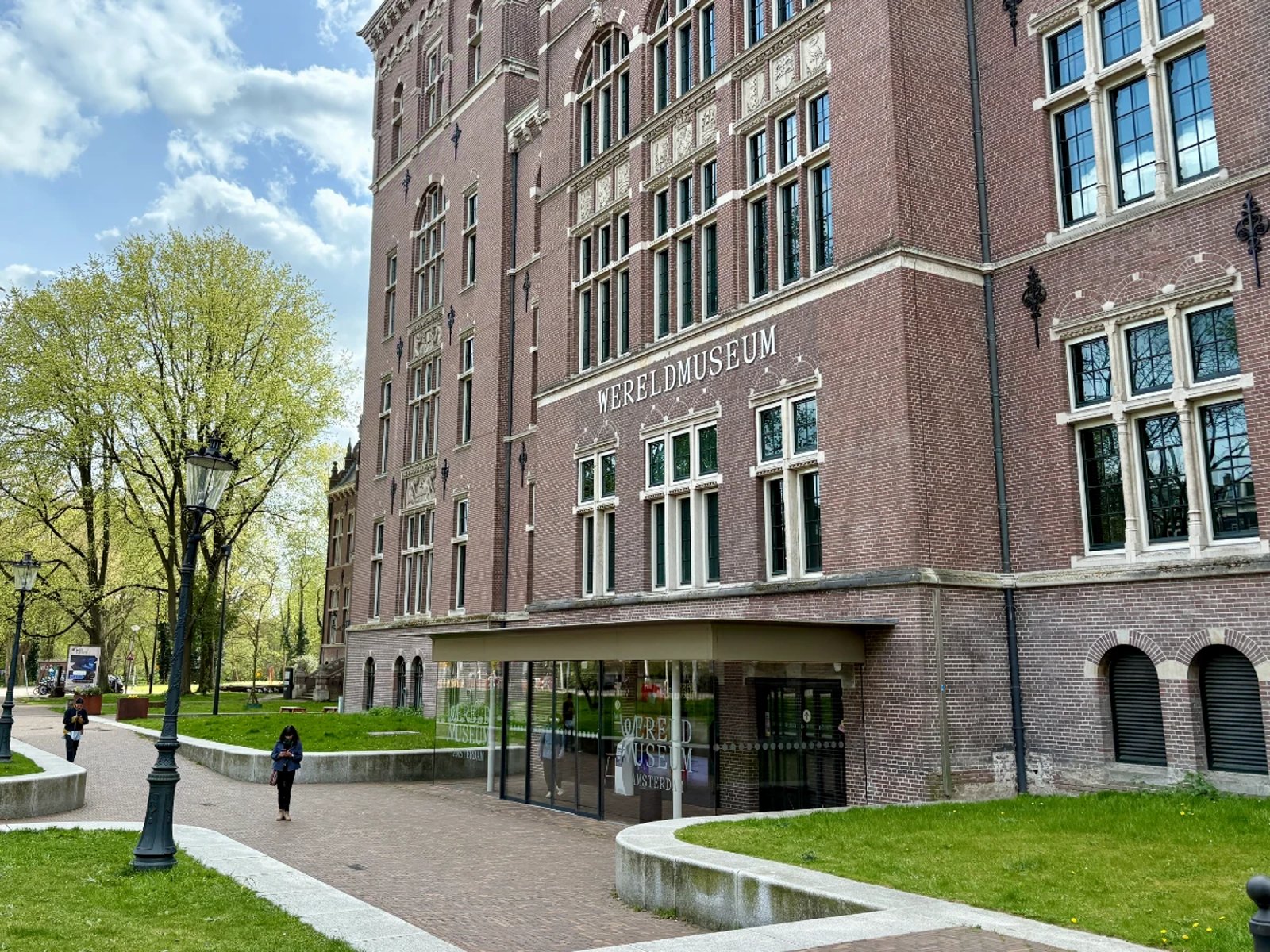 Stately brick museum building with modern glass entrance and grassy lawn and trees in front