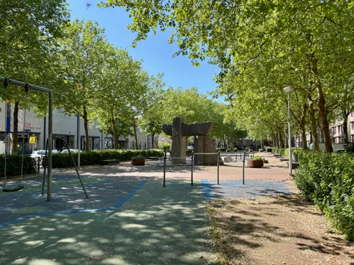 Shaded playground with swing, bars, and large stone sculpture