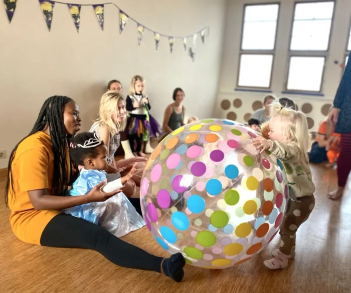 Parents and kids sitting on the floor playing with a giant rainbow polka dot beach ball