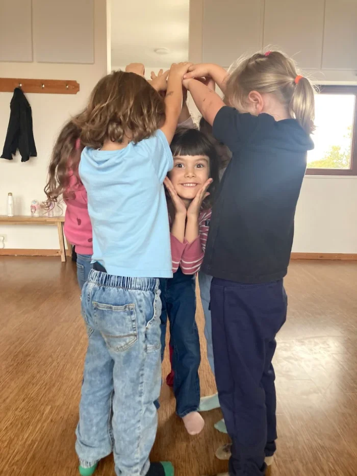 Kids making a teepee with their hands while a young girl pokes her head out to smile at the camera