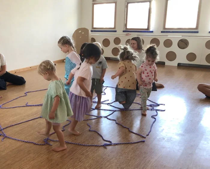 Several toddlers playing a game in a dance studio with purple rope on the ground