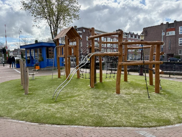 Wooden climbing structure with nets and ladders and bright blue coffee kiosk and buildings behind