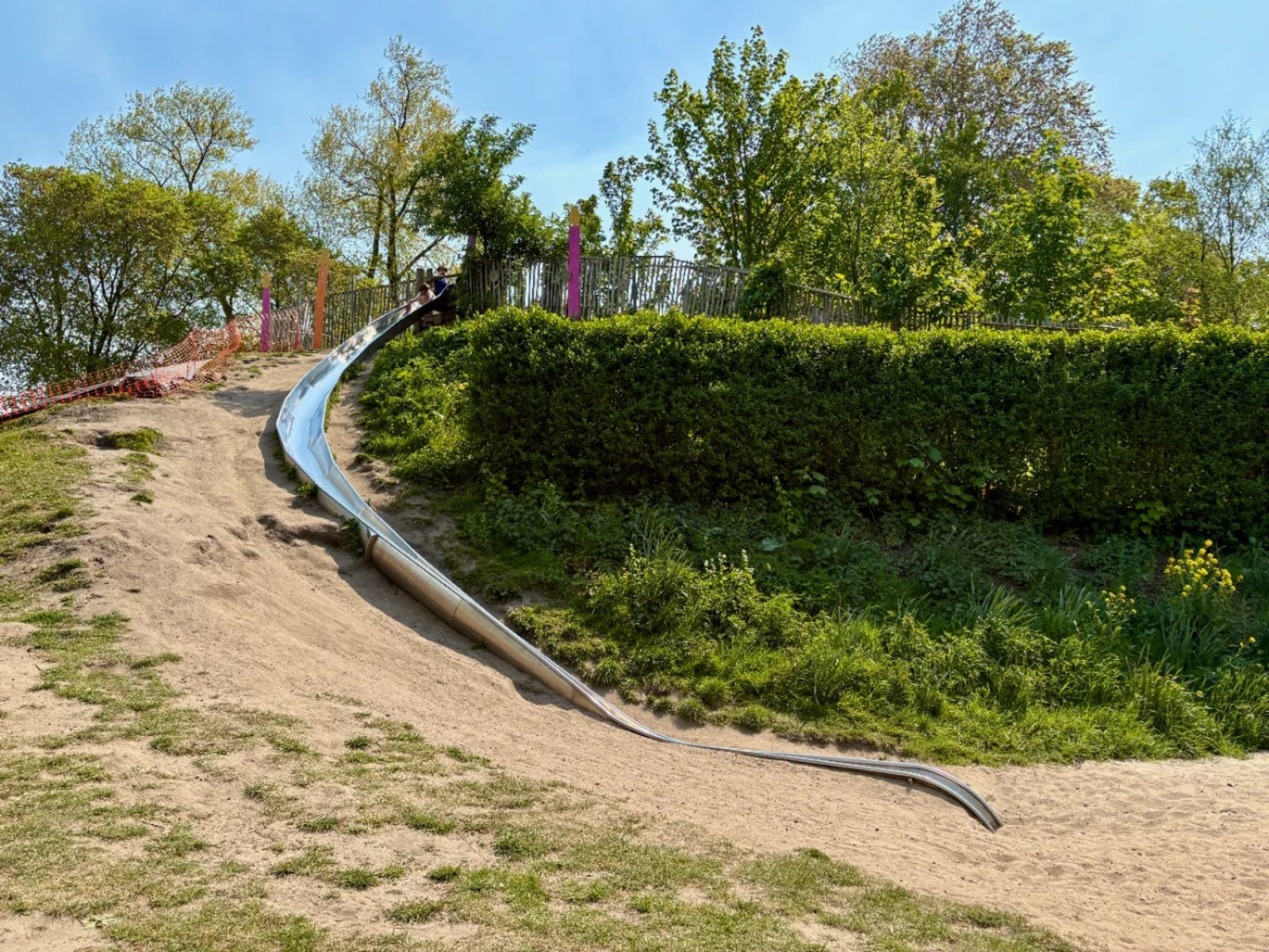 Long, curving metal slide set on a hill with grass and dirt around