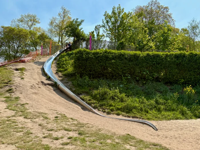 Long, curving metal slide set on a hill with grass and dirt around