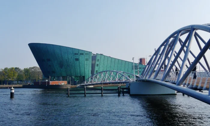 Modern museum building in green metal cladding with steel bridge connecting to it over water