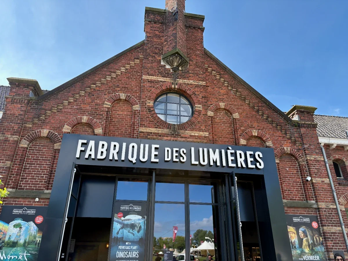 Historic brick building with ornate details and large black steel portal storefront with posters and FABRIQUE DES LUMIERES written above entrance