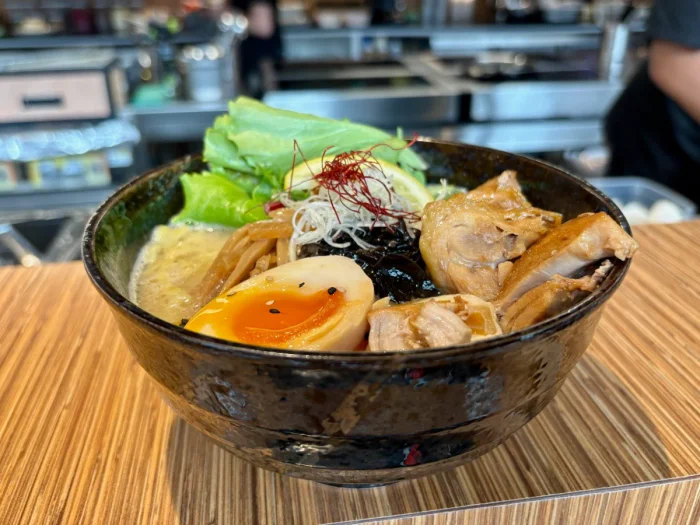 Bowl of ramen on a wooden counter with chicken, lettuce, an egg, and seaweed
