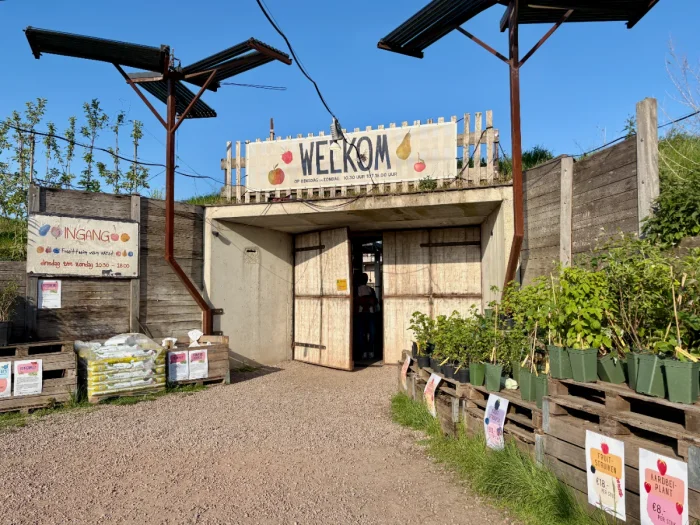 Entrance to a farm with plants for sale outside, large barn doors, and a big WELKOM sign above