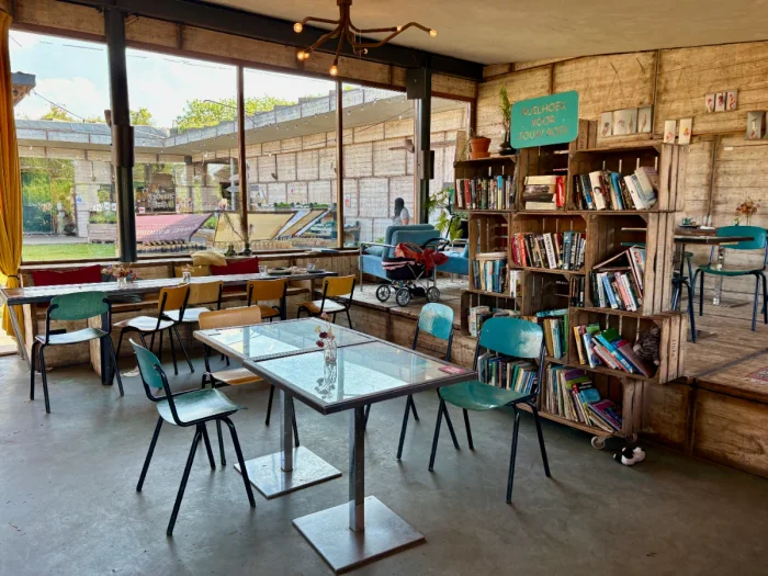 Inside of a cafe with large bookshelf separating two spaces and tables and chairs and large windows looking outside