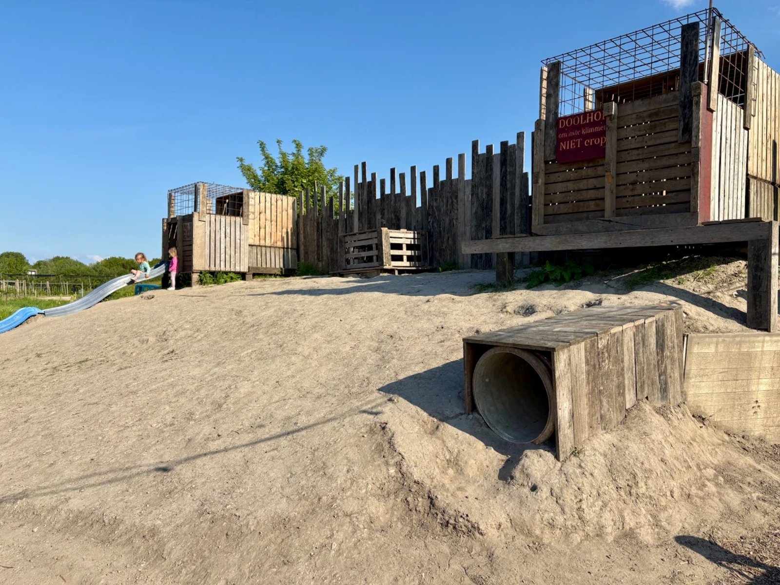 Rustic playground built into a dirt hill with tunnels, crates, and a slide