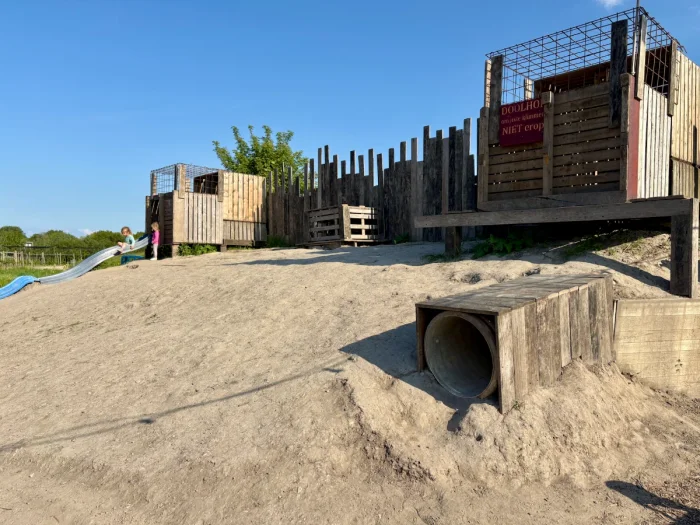 Rustic playground built into a dirt hill with tunnels, crates, and a slide