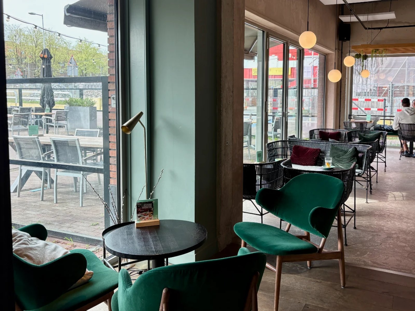 Cafe with cozy velvet chairs and black wicker furniture and large windows overlooking terrace seating area