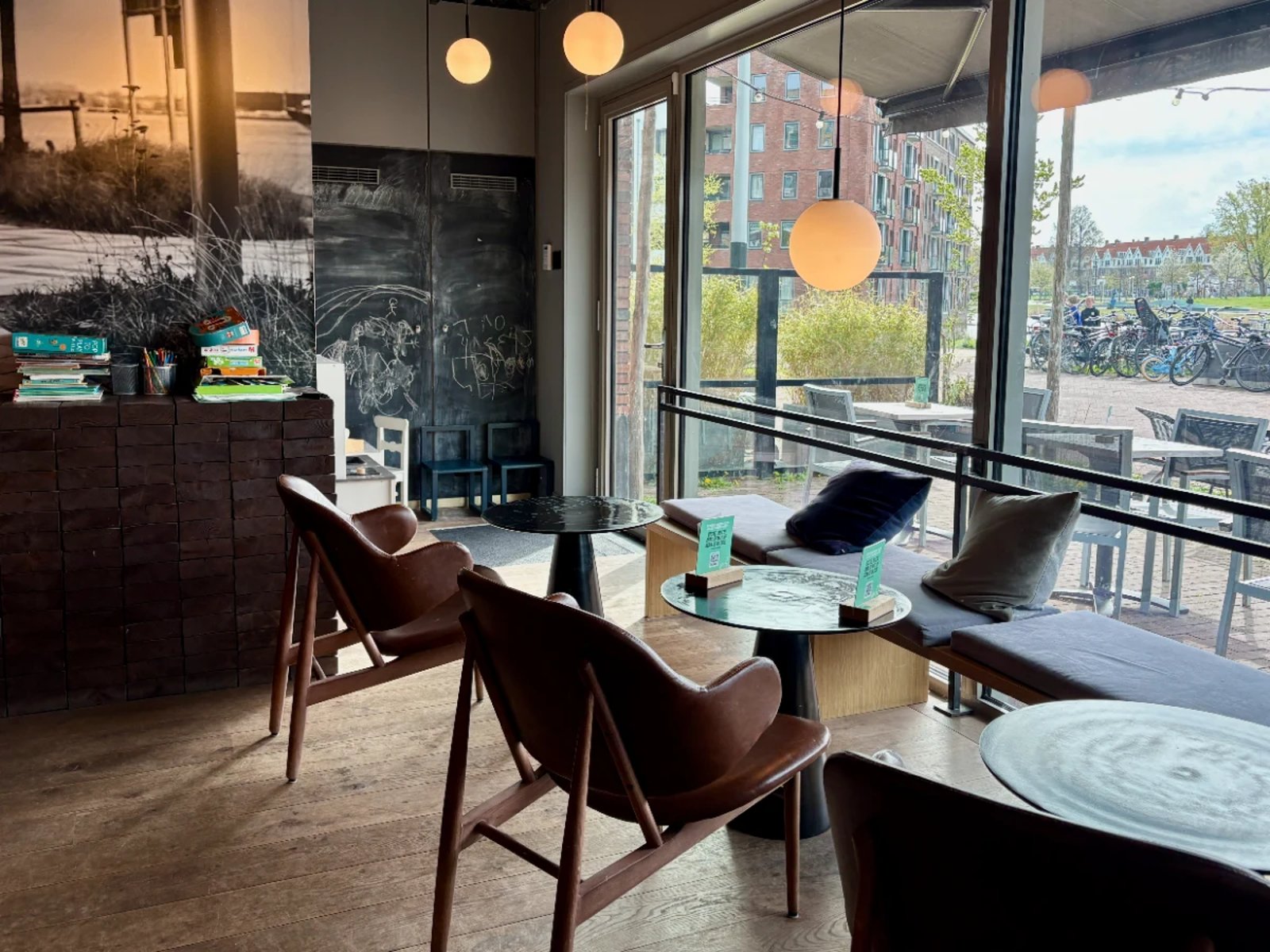 Cafe seating with leather chairs and bench below large windows with children's play corner, toys, and books beside