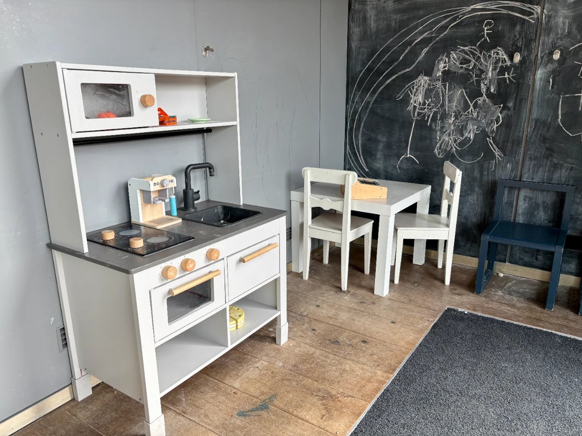 Children's play corner with white play kitchen, table and chairs, and chalk wall