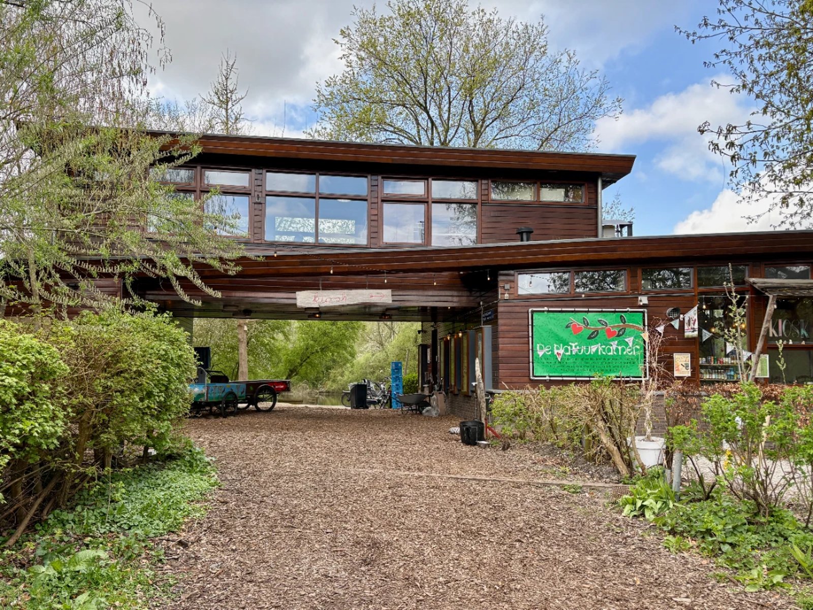 Community center building spanning pathway through park with large green sign