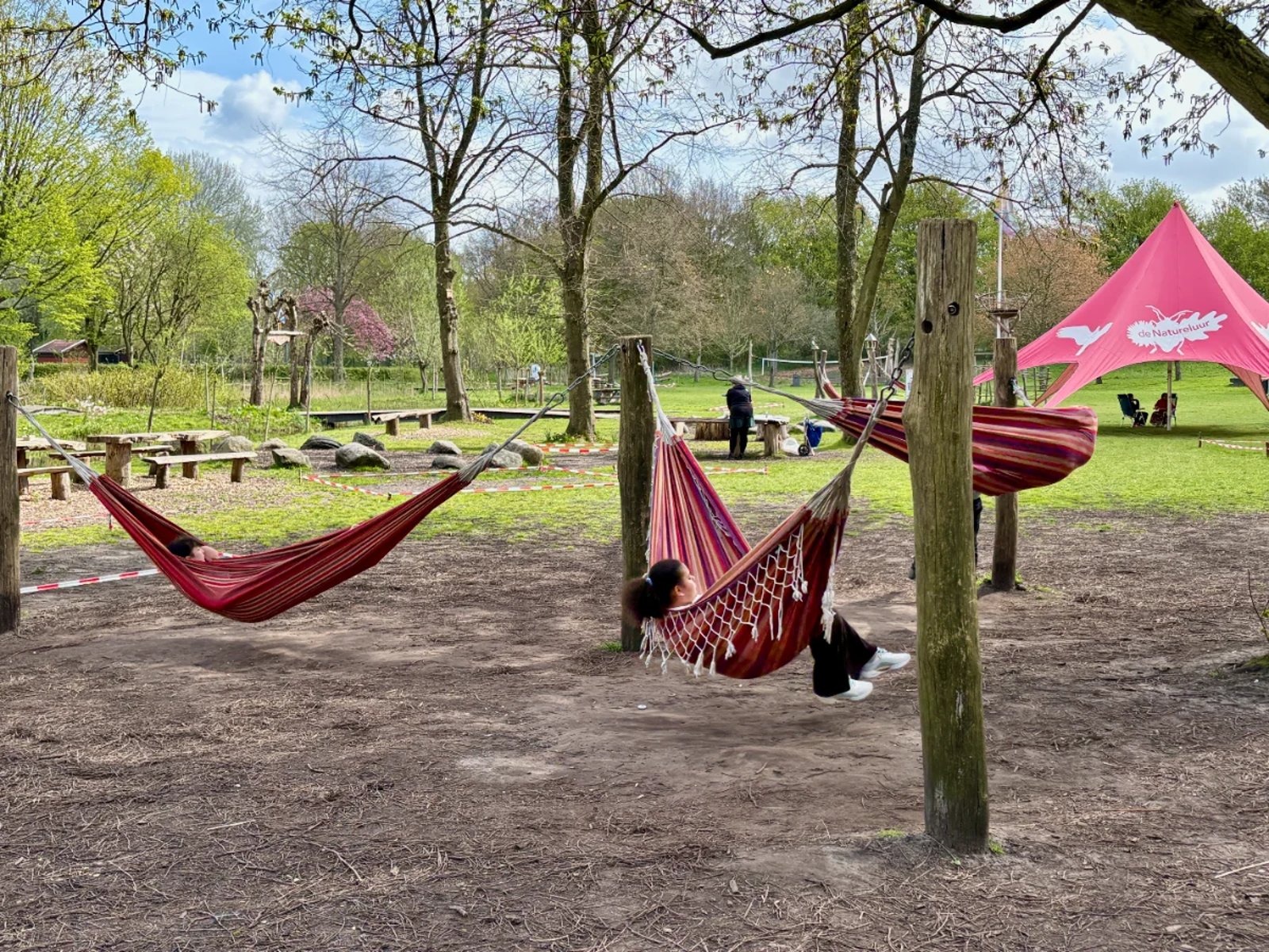 Three kids swinging in red hammocks with grassy lawn and large, red tent behind