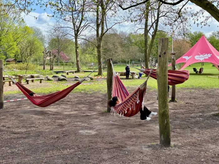Three kids swinging in red hammocks with grassy lawn and large, red tent behind